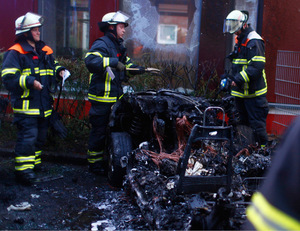 Feuerwehrleute begutachten die Überreste eines ausgebrannten Autos.